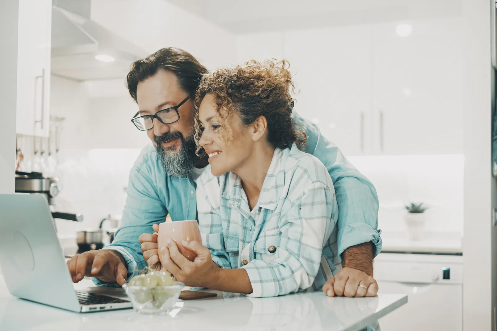 A smiling couple reviewing financing options on a laptop in their kitchen