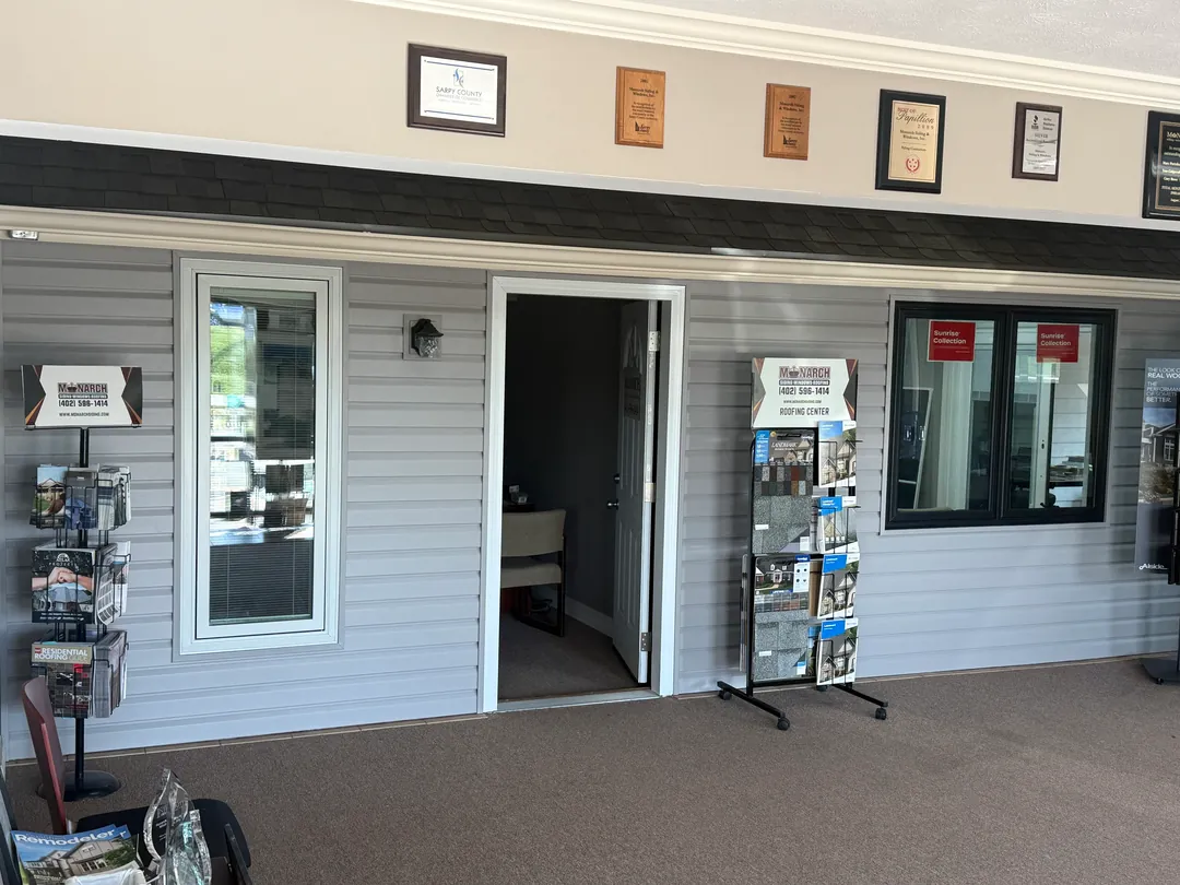 Mock house front in the Monarch showroom with siding, windows and an entry door, award plaques above