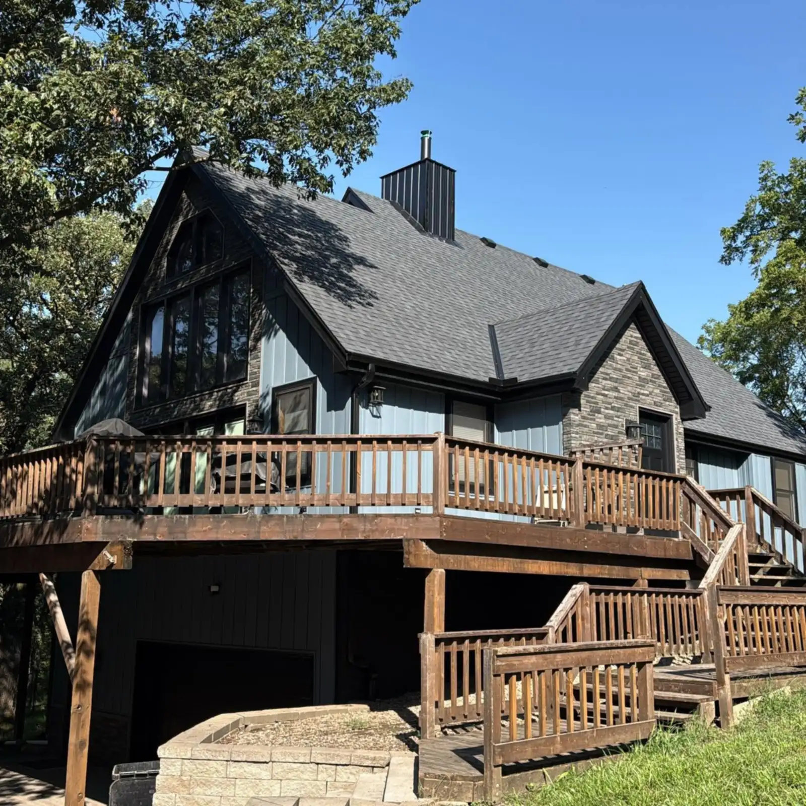 A home with blue board-and-batten siding, stone accents and a wraparound deck