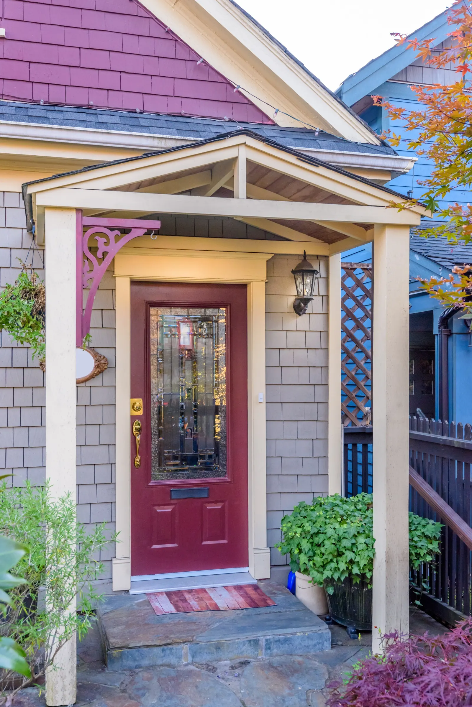 A burgundy entry door with a decorative glass panel under a covered porch