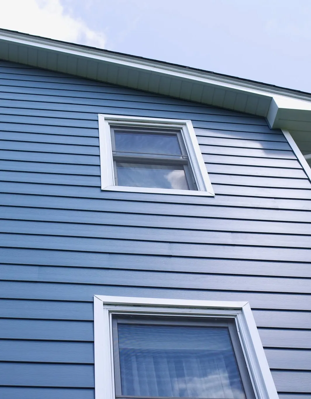 A window with wrapped trim on blue lap siding